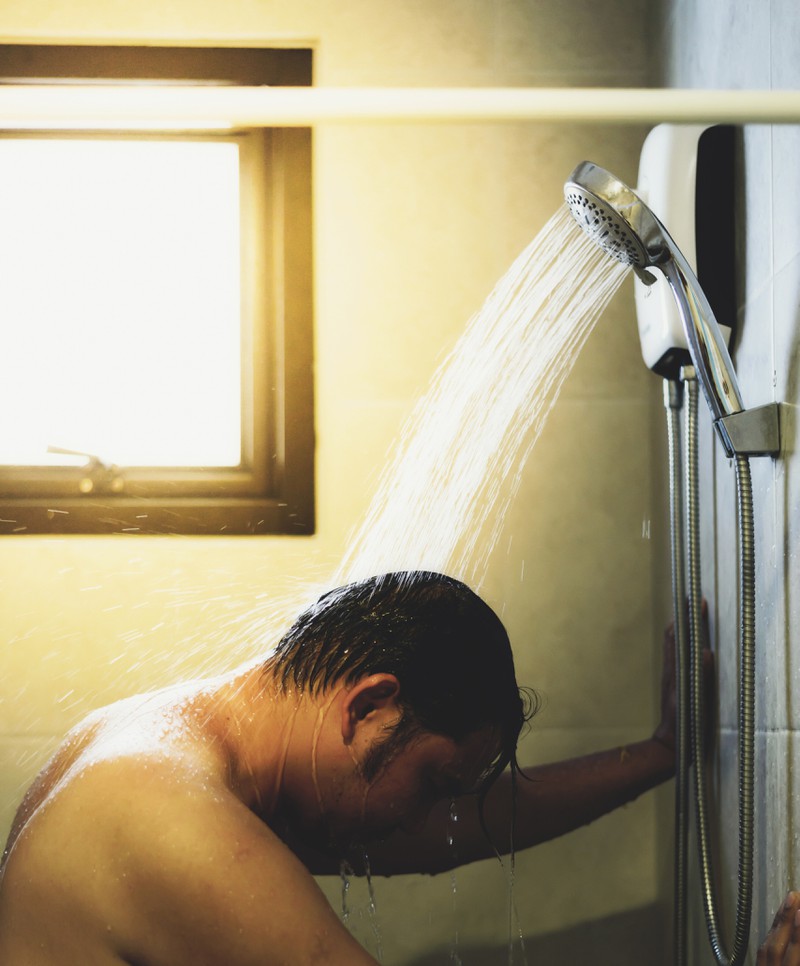 Ein Mann begutachtet seinen Intimbereich unter der Dusche