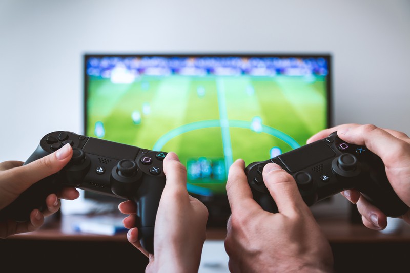 zwei playstation kontroller, tv im hintergrund fußball