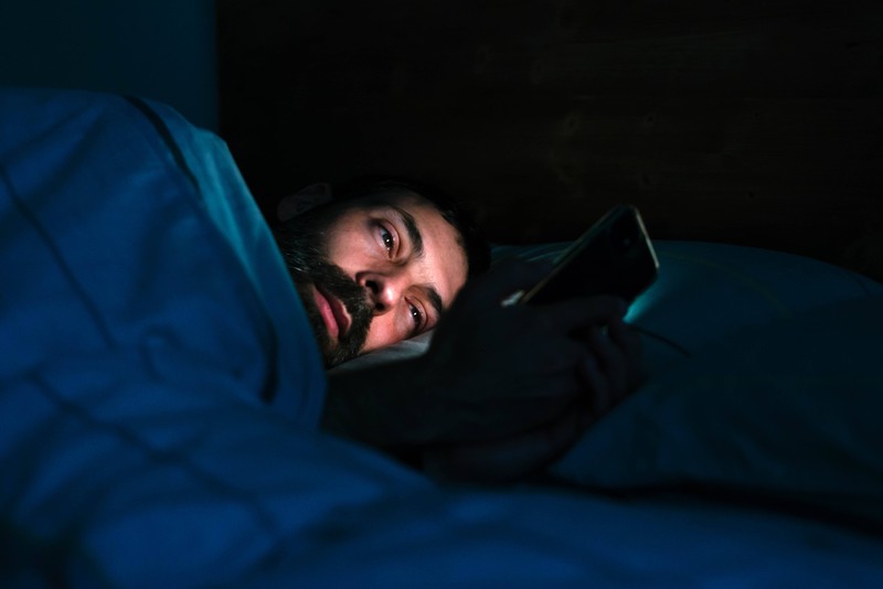 Ein Mann liegt im Bett und schaut auf sein Smartphone