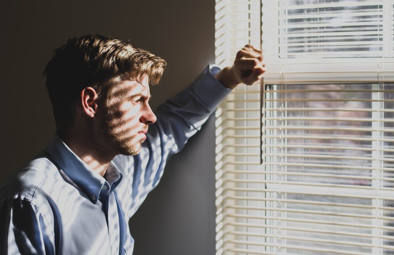 Mann starrt traurig aus dem Fenster. ER könnte Hodenkrebs haben was ein Grund für starke Hodenschmerzen sein kann
