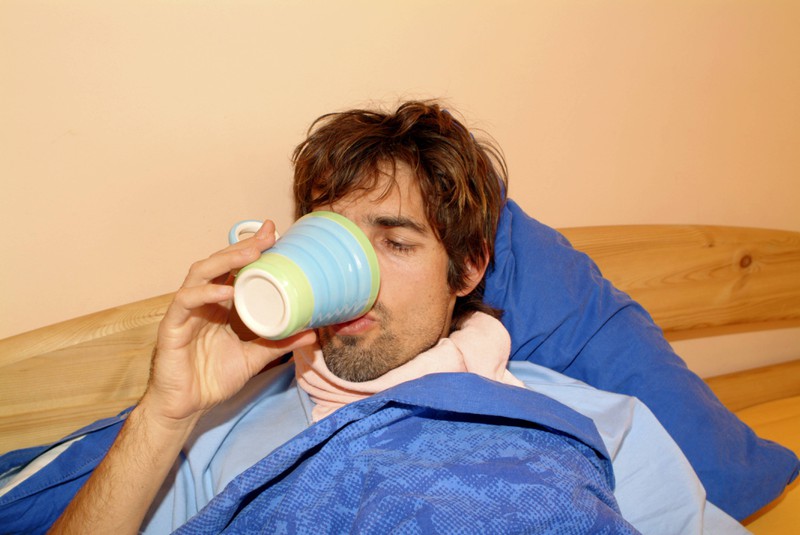 Ein Mann liegt im Bett und trinkt Tee gegen seine Erkältung