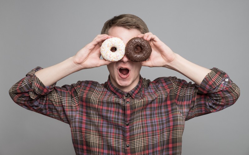 Zu sehen ist ein Mann, der sich zwei Donuts vor die Augen hält.