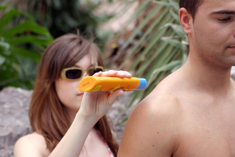 Junge Frau cremt ihrem Freund den Rücken mit Sonnenmilch ein