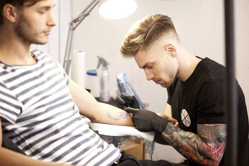 Ein Tätowierer, der einem Mann ein Tattoo sticht